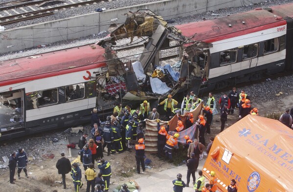 FILE - Rescue workers cover bodies alongside a bomb-damaged passenger train, following a number of explosions in Madrid, Spain, on March 11, 2004. Victims of terror attacks are a symbol of the constant need to guard freedom and the rule of law against threats, King Felipe VI of Spain said Monday March 11, 2024 at a ceremony marking the 20th anniversary of one of Europe’s deadliest extremist attacks. (AP Photo/Paul White, File)
