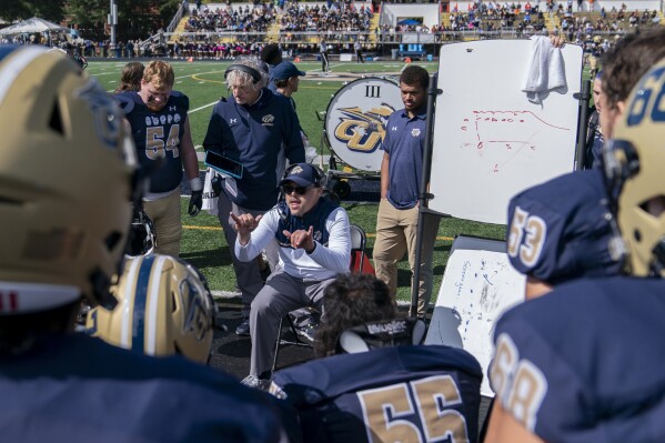 Gallaudet head coach Chuck Goldstein, center, uses American Sign Language to communicate with players during an NCAA college football game against Hilbert College, Saturday, Oct. 7, 2023, in Washington. Since arriving at Gallaudet as an assistant in 2009 just as his next job, Goldstein has embraced coaching a team of deaf and hard-of-hearing players and the adjustments that go with it. He learned ASL as the primary method of communication. During games, he still worries about opponents being injured because his players can't hear whistles. (AP Photo/Stephanie Scarbrough)