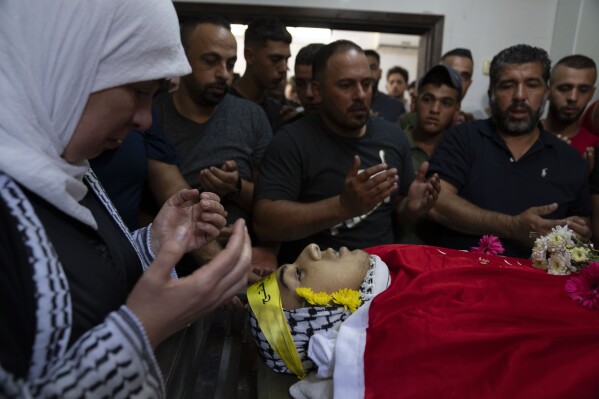 Mourners pray over the body of Ramzi Hamed, 17, during his funeral in the West Bank city of Ramallah, Monday, Aug. 7, 2023. Ramzi Hamed, who was shot by Israeli troops last week after throwing a firebomb at soldiers in the occupied West Bank died Monday, the Palestinian Health Ministry said. (AP Photo/Nasser Nasser)