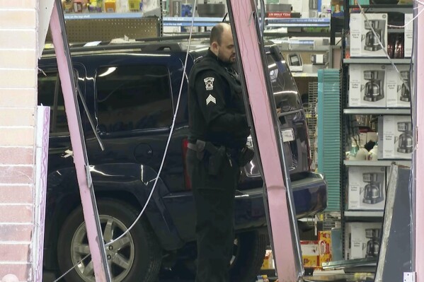 In this photo made from video, a police officer stands in front of a vehicle that crashed into a Walmart store in Canton Township, Mich., on Friday, March 1, 2024 . A sport-utility vehicle crashed into a Walmart in suburban Detroit, injuring several people Friday afternoon, police said.(AP Photo/Mike Householder)