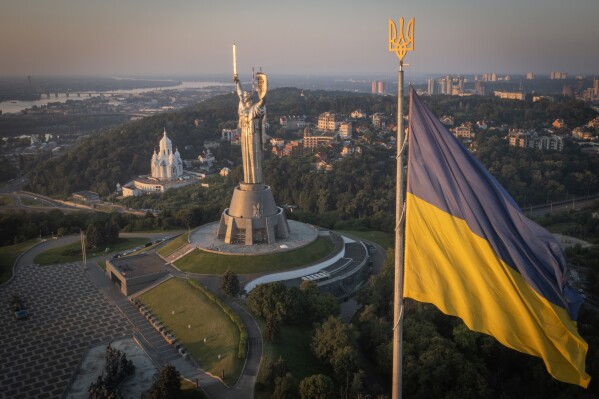 The national flag waves as workers install the Ukrainian coat of arms on the shield in the hand of the country's tallest stature, the Motherland Monument, after the Soviet coat of arms was removed, in Kyiv, Ukraine, Sunday, Aug. 6, 2023. Ukraine is accelerating efforts to erase the vestiges of centuries of Soviet and Russian influence from the public space amid the Russian invasion of Ukraine by pulling down monuments and renaming hundreds of streets to honor home-grown artists, poets, military chiefs, and independence leaders. (AP Photo/Efrem Lukatsky)