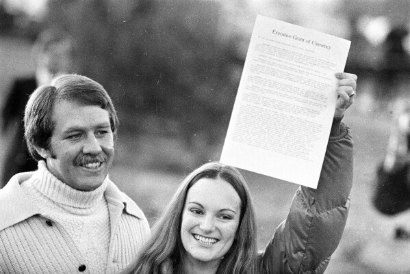FILE - A happy Patricia 鈥淧atty鈥� Hearst displays the executive grant of clemency as she leaves the Federal Correctional Institution in Pleasanton, Calif., Feb. 2, 1979. With her is fiance Bernard Shaw, her former bodyguard. The newspaper heiress was kidnapped at gunpoint on Feb. 4, 1974, by the Symbionese Liberation Army, a little-known armed revolutionary group. The 19-year-old college student's infamous abduction in Berkeley, Calif., led to Hearst joining forces with her captors for a 1974 bank robbery that earned her a prison sentence. Hearst, granddaughter of wealthy newspaper magnate William Randolph Hearst, will turn 70 on Feb. 20. (APPhoto/File)