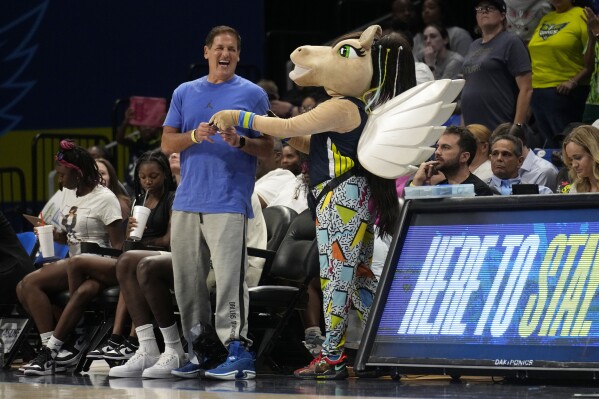 Dallas Mavericks team owner Mark Cuban, center left, laughs as he interacts with Dallas Wings mascot "Lightning" during the second half of a WNBA basketball game against the Minnesota Lynx, Thursday, Aug. 24, 2023, in Arlington, Texas. (AP Photo/Tony Gutierrez)