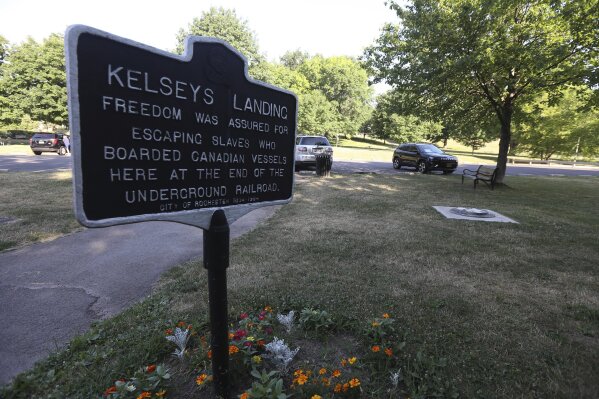 A sign marking a historic Underground Railroad spot sits near the base of a statue of Frederick Douglass which is all that remains, Monday, July 6, 2020 in Rochester, N.Y., after it was found vandalized in Maplewood Park. Police say the statue of Douglass was taken from Maplewood Park and placed near the Genesee River gorge on Sunday. This site includes Kelsey's Landing, a part of the Underground Railroad, where Douglass, Harriet Tubman and others helped slaves get to freedom via the Genesee River located below adjacent gorge. (Tina MacIntyre-Yee/Rochester Dem via AP)