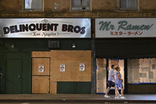 A couple walks past boarded up businesses along 1st St. in Little Tokyo Tuesday, June 17, 2025, in Los Angeles. (AP Photo/Wally Skalij)