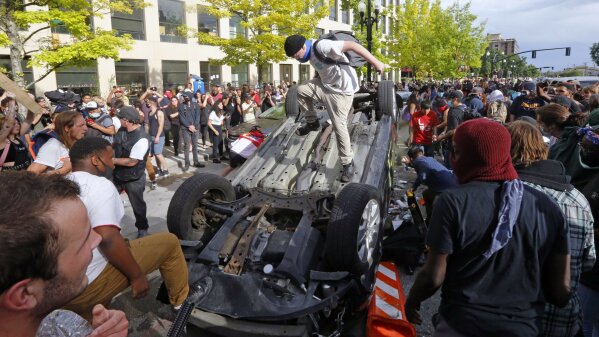 FILE - In this Saturday, May 30, 2020, photo, protesters jump on a flipped vehicle, in Salt Lake City. Protests in Salt Lake City that drew several thousand people are a setback for contact tracers already struggling to contain the spread of the coronavirus, said Tair Kiphibane, infectious disease bureau manager for the Salt Lake County Health Department. (AP Photo/Rick Bowmer, File)