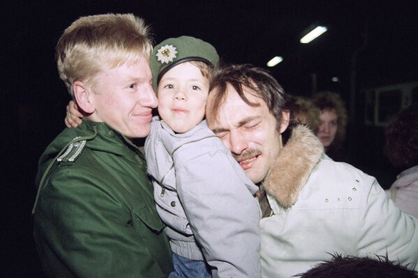 Heinz Joachim Nickel, right, a member of the East German opposition group "New Forum," is overcome with emotion as he and his son, Christian, center, arrive in Helmstedt, West Germany by train from East Germany, Nov. 11, 1989. Christian wears a cap belonging to an unidentified West German border guard, left. Nickel said he and his son will return to East Germany. (AP Photo/Claus Eckert)