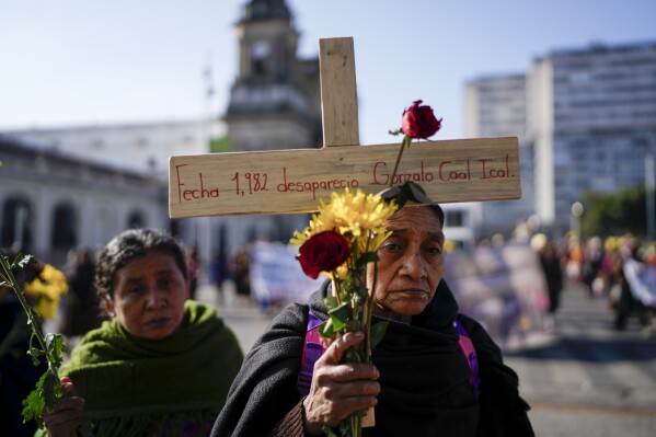 An Indigenous woman carries a cross with the name of a missing person during a memorial for the victims of the civil war in Guatemala City, Feb. 25, 2024. (AP Photo/Moises Castillo)