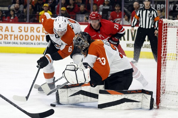 Philadelphia Flyers goaltender Samuel Ersson (33) controls the puck with Travis Sanheim (6) and Carolina Hurricanes' Stefan Noesen (23) nearby during the second period of an NHL hockey game in Raleigh, N.C., Thursday, March 21, 2024. (AP Photo/Karl B DeBlaker)