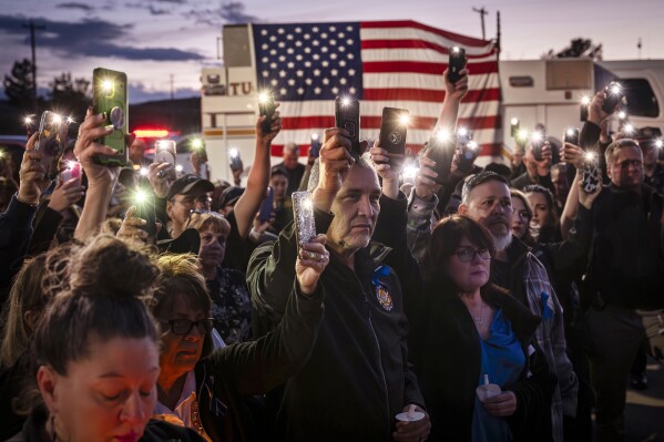 People raise their phone flashlights in honor of New Mexico State Police Officer Justin Hare during a vigil at the New Mexico State Police Office in Tucumcari, N.M., on Wednesday, March 20, 2024. Hare was fatally shot while on duty Friday, March 15, west of Tucumcari. (Chancey Bush/The Albuquerque Journal via AP)