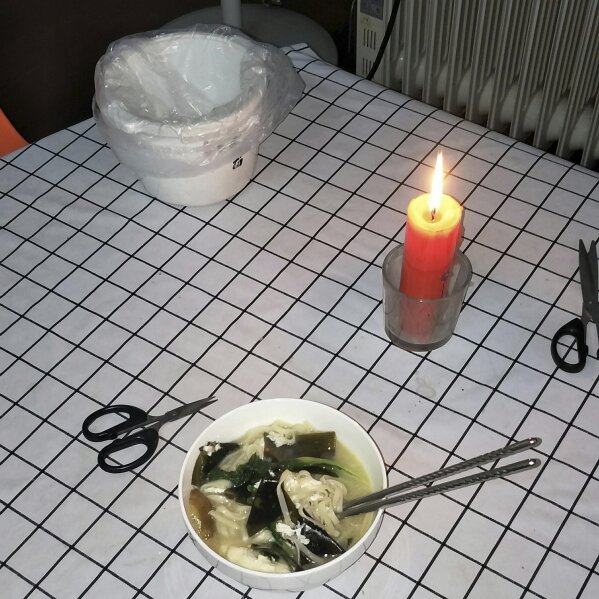 This photo provided by Zhong Hanneng shows a candle she lit in memory of her son, Peng Yi, during a meal of noodles at her home in Wuhan, China, in July 2020. Peng first started coughing on Jan. 23 at the beginning of the coronavirus outbreak, but because of a shortage of test kits, he wasn't able to get tested for days. His first test result came out negative, barring him access to a hospital bed, and he wasn't able to be hospitalized until weeks later. By then his condition was critical, and he passed away on Feb. 19. (Zhong Hanneng via AP)