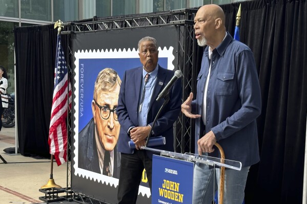 Jamaal Wilkes, left, listens as Kareen Abdul-Jabbar speaks at the first-day-of-issue ceremony for the John Wooden forever stamp on the UCLA campus in Los Angeles, Calif., on Saturday, Feb. 24, 2024. Wilkes and Abdul-Jabbar both played for Wooden, who coached UCLA to a record 10 national basketball championships. Wooden died in 2010 at age 99. (AP Photo/Beth Harris)