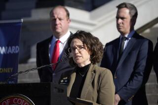 FILE - Colorado Governor Jared Polis, back left, and Colorado Senate Majority Leader Steve Fenberg, back right, listen as Majority Leader Daneya Esgar speaks during a news conference on the west steps of the State Capitol about legislative plans for the upcoming session in this file photograph taken Monday, Jan. 10, 2022, in Denver, Colorado. (AP Photo/David Zalubowski, File)