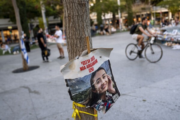 A poster depicting Israeli hostage Noa Argamani, 26, is displayed next to a memorial in Tel Aviv on Thursday, April 4, 2024. Argamani was kidnapped to Gaza on Oct. 7 during the cross-border attack by Hamas militants at the Nova music festival near Kibbutz Re’im, southern Israel. Half a year into Israel's war, agonized families are in a race against time. In November, a weeklong cease-fire deal saw the release of more than 100 hostages. But the war is dragging on, with no end in sight and no serious hostage deal on the table. (AP Photo/Oded Balilty)