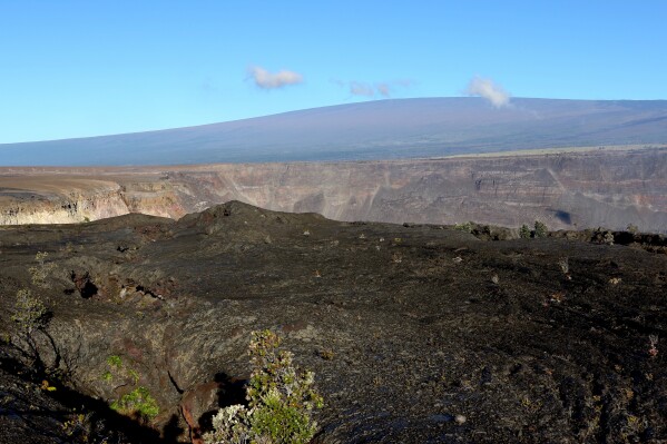 FILE - Hawaii's Mauna Loa volcano, background, towers over the summit crater of Kilauea volcano in Hawaii Volcanoes National Park on the Big Island on April 25, 2019. A magnitude 5.7 earthquake struck the world's largest active volcano Friday, Feb. 9, 2024, Mauna Loa on the Big Island of Hawaii, knocking items off shelves in nearby towns but not immediately prompting reports of serious damage. (AP Photo/Caleb Jones, File)