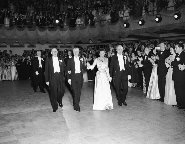 The Duke and Duchess of Windsor, Prince Edward and Wallis Simpson, center, are escorted around the floor at the ball of Rex by two members of the organization in New Orleans, Louisiana on Feb. 21, 1950. Guests applaud the royal British couple who were making their first appearance at a Mardi Gras ball. (AP Photo, file)