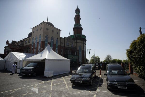 In this photo taken on Friday, April 24, 2020, a volunteer wearing protective clothing and a face mask to protect from coronavirus, walks through the car park of Central Jamia Mosque Ghamkol Sharif in Birmingham, England. The holy month of Ramadan is underway, and the Central Jamia Mosque Ghamkol Sharif should be full of worshippers. But this year, the main arrivals are the dead. While the mosque in the central England city of Birmingham has been closed in response to the coronavirus pandemic, its parking lot has been transformed into a temporary morgue with room for 150 bodies. (AP Photo/Matt Dunham)