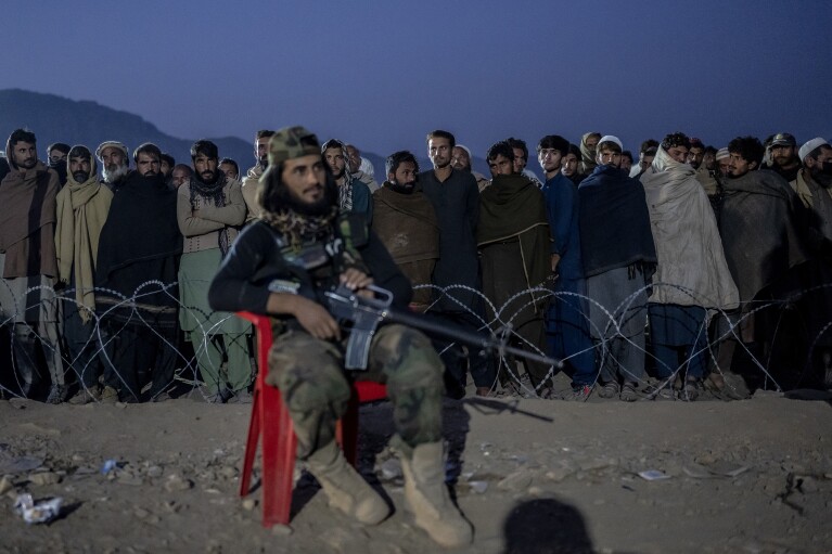 A Taliban fighter stands guard as Afghan refugees line up to register in a camp near the Pakistan-Afghanistan border in Torkham, Afghanistan, Saturday, Nov. 4, 2023. (AP Photo/Ebrahim Noroozi)