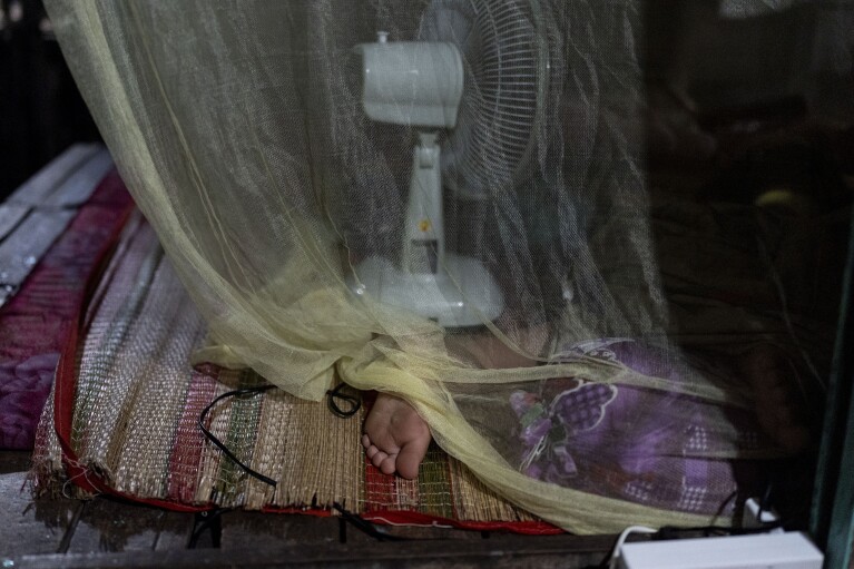Do Hoang Trung, who lives on a houseboat with his twin sister and their grandmother, sleeps under a mosquito net in Can Tho, Vietnam, Wednesday, Jan. 17, 2024. After their mother left to pursue better opportunities in Ho Chi Minh City, Trung and his sister remained in the care of their grandmother, who supports the family by selling steamed buns at a floating market. (AP Photo/Jae C. Hong)