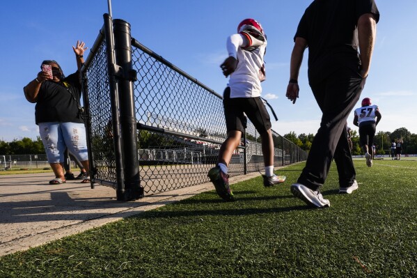 Families wave and take photos as members of the Clinton High School freshman football team arrive for a game at Brandon High in Brandon, Miss., Tuesday, Aug. 27, 2024. (AP Photo/Gerald Herbert)