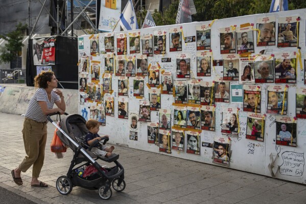 Passersby observe the photos of hostages held in the Gaza Strip that are plastered to the walls of a plaza known as Hostages Square in Tel Aviv, Israel, Friday, May 17, 2024. The Israeli military said Friday its forces rescued from Gaza the remains of three Israeli hostages taken by militants during the Oct. 7 attack, including 22-year-old German-Israeli Shani Louk, 28-year-old Amit Buskila, and 56-year-old Itzhak Gelerenter. (AP Photo/Oded Balilty).