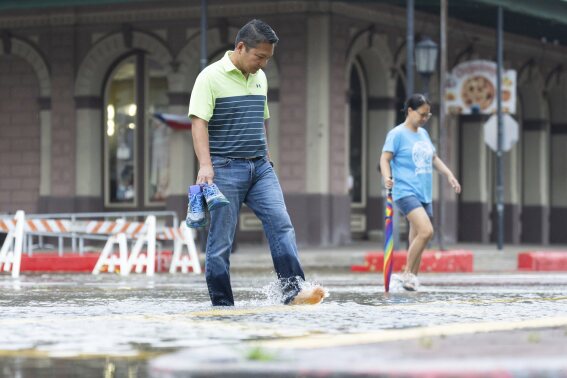 Roy Quiroz y su esposa, Minda, caminan por una calle inundada mientras llueve el miércoles 19 de junio de 2024, en Galveston, Texas. La tormenta tropical Alberto se formó en el suroeste del Golfo de México, la primera tormenta con nombre de lo que se prevé que sea una agitada temporada de huracanes. (Jason Fochtman/Houston Chronicle vía AP)