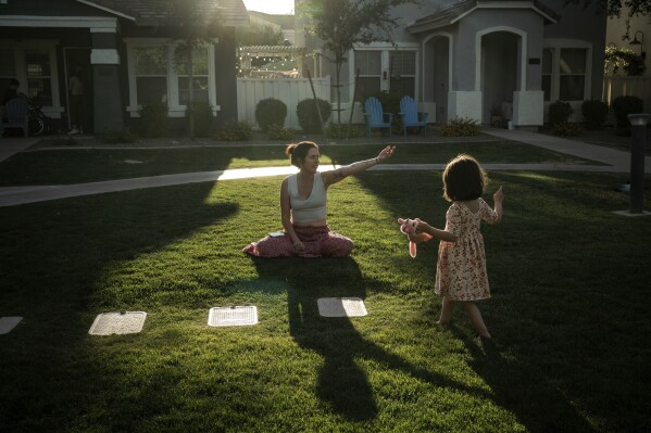 Maria Padron, center, plays with her daughter Fae Padron, 4, right, in a "kid pod," a cluster of families with more than 20 kids between them, at Agritopia, a community nestled around a plot of agricultural land, April 21, 2025, in Gilbert, Ariz. (AP Photo/Annika Hammerschlag)