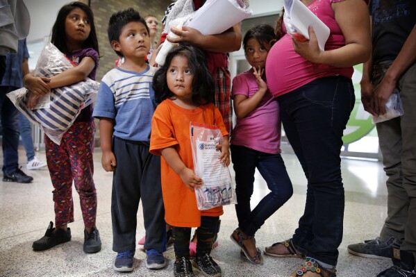 FILE - Ingrid Yanet Lopez Hernandez, 32, center back, her children, from left, Jazmine, 7, Christian, 5, and Cristle Ordonez, 2, and pregnant mother Meregilda Mejilla, 27, and her daughter Maricelda Mejilla, 6, wait for transportation to Catholic Charities of the Rio Grande Valley after being processed by the U.S. Border Patrol in McAllen, Texas, on June 24, 2018. (Tom Fox/The Dallas Morning News via ĢӰԺ, File)