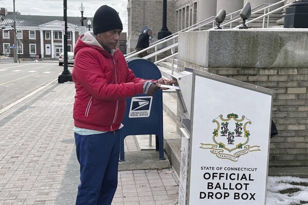 FILE - Manuel Alcantara deposits absentee ballots for his son and daughter in a dropbox outside City Hall in Bridgeport, Conn., Wednesday, Feb. 21, 2024. (AP Photo/Susan Haigh, File)
