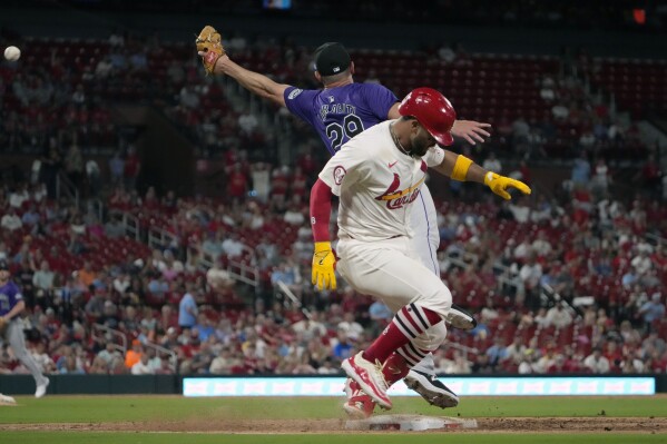 St. Louis Cardinals' Ivan Herrera, front, is safe at first on a throwing error by Colorado Rockies shortstop Ezequiel Tovar as Rockies relief pitcher Matt Carasiti reaches for the throw during the sixth inning of a baseball game Thursday, June 6, 2024, in St. Louis. The Cardinals' Nolan Gorman scored on the play. (AP Photo/Jeff Roberson)