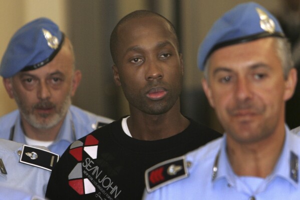 FILE - Rudy Hermann Guede, center, is escorted by Italian penitentiary police officers as he leaves Perugia's court, Italy, Friday, Sept. 26, 2008. Guede was convicted for the slaying of Meredith Kercher in Perugia, Italy, where she was studying and sharing an apartment with U.S. student Amanda Knox. Guede has denied killing Kercher. Amanda Knox faces yet another trial for slander in a case that could remove the last remaining guilty verdict against her eight years after Italy's highest court definitively threw out her conviction for the murder of her 21-year-old British roommate, Meredith Kercher. (AP Photo/Pier Paolo Cito, File)