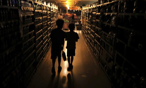 FILE - Elijah Carter 11, left, and Robert Haralson, 12, help shop for their parents in a darkened Olivers Supermarket in the Rincon Valley community in Santa Rosa, Calif., Oct. 23, 2019. Weather disasters fueled by climate change now roll across the U.S. year-round, battering the nation's aging electric grid. (Kent Porter/The Press Democrat via AP, File)