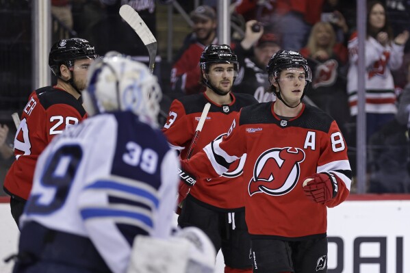 New Jersey Devils center Jack Hughes, right, reacts after scoring a goal past Winnipeg Jets goaltender Laurent Brossoit during the second period of an NHL hockey game Thursday, March 21, 2024, in Newark, N.J. (AP Photo/Adam Hunger)
