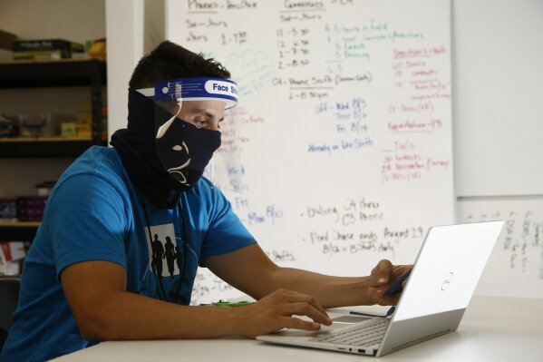 FILE - In this Aug. 6, 2020 file photo wearing a face covering and face shield while working amid the coronavirus, Maico Olivares, lead voter registration organizer for Central Arizonans for a Sustainable Economy, works his phone and computer as he tries to reach about 25 people a day, mostly within the Latino community, to persuade them to register to vote, in Phoenix. Immigrant-rights and grassroots organizations that have been mobilizing Latinos in Arizona for nearly two decades helped propel Joe Biden to victory in a traditionally conservative state.  (AP Photo/Ross D. Franklin,File)