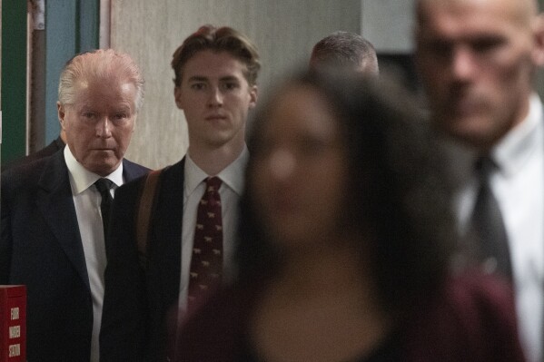 Musician Don Henley, left, surrounded by security, arrives at the Supreme Court to testify, Monday, Feb. 26, 2024, in New York.  The judgment surrounding pages of draft lyrics for "Hotel California" and other Eagles hits will feature a star witness: Don Henley.  The Eagles co-founder is scheduled to testify Monday in the criminal trial of three collection professionals.  (AP Photo/Mary Altaffer)