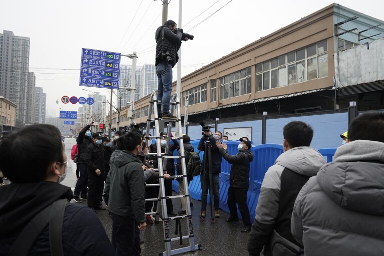FILE - A photographer on a tall ladder tries to take photos of the World Health Organization convoy after it entered the Huanan Seafood Market on the third day of field visit in Wuhan in central China's Hubei province on Jan. 31, 2021. The hunt for COVID-19 origins has gone dark in China. An AP investigation drawing on thousands of pages of undisclosed emails and documents and dozens of interviews found feuding officials and fear of blame ended meaningful Chinese and international efforts to trace the virus almost as soon as they began, despite years of public statements to the contrary. (AP Photo/Ng Han Guan, File)