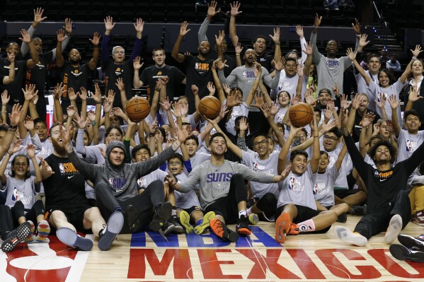 FILE - Phoenix Suns' players and coaches pose with young athletes following an NBA Cares basketball clinic, a day before their regular-season NBA game against the San Antonio Spurs in Mexico City, Friday, Dec. 13, 2019. The NBA has announced the Atlanta Hawks and Orlando Magic will play a regular-season game in Mexico City on Nov. 9. It will be the 32nd NBA game in Mexico since 1992. (AP Photo/Rebecca Blackwell, File)