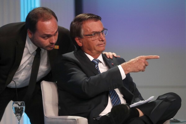 FILE - Carlos Bolsonaro, son of Brazil's President Jair Bolsonaro who is running for re-election, whispers in his father's ear during his arrival at the presidential debate in Rio de Janeiro, Brazil, Sept. 29, 2022. Brazil's federal police carried out a search warrant Jan. 29, 2024 for Carlos Bolsonaro, a Rio de Janeiro city councilman, an officer with knowledge of the operation told The Associated Press. (AP Photo/Bruna Prado)