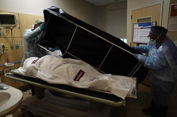 FILE - In this Jan. 9, 2021 file photo, transporters Miguel Lopez, right, Noe Meza prepare to move a body of a COVID-19 victim to a morgue at Providence Holy Cross Medical Center in the Mission Hills section of Los Angeles. The U.S. death toll from COVID-19 has topped 600,000, even as the vaccination drive has drastically slashed daily cases and deaths and allowed the country to emerge from the gloom. (AP Photo/Jae C. Hong, File)