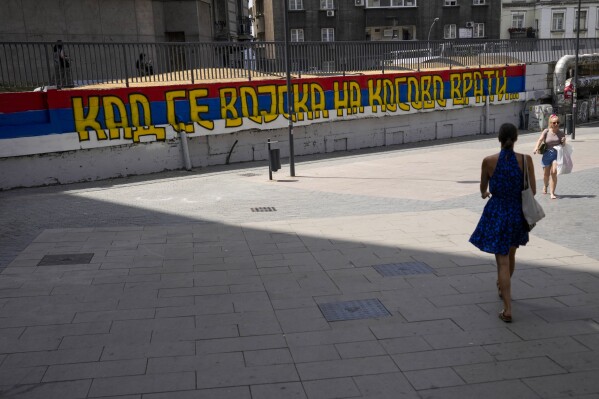 People walk past a mural painted in colours of the Serbian flag, that reads: 