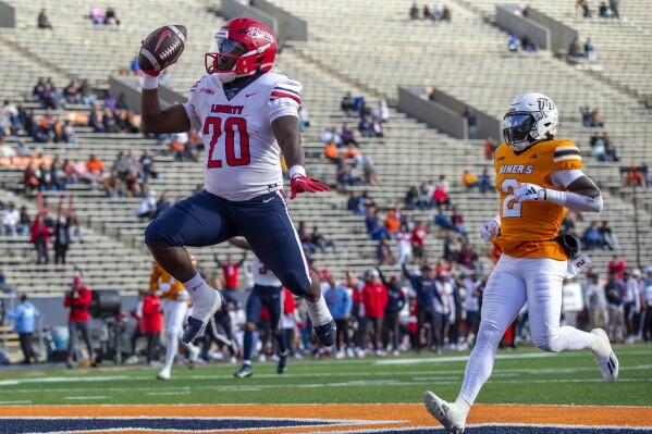 Liberty running back Quinton Cooley (20) celebrates after scoring a touchdown ahead of UTEP safety Kobe Hylton (2) during the first half of an NCAA college football game on Saturday, Nov. 25, 2023, in El Paso, Texas. (AP Photo/Andres Leighton)