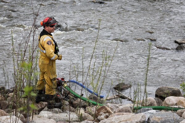 A firefighter monitors a pump in a river bed used for wildfire sprinklers in the evacuated neighbourhood of Grayling Terrace in Fort McMurray, Alta., Thursday, May 16, 2024. (Jeff McIntosh/The Canadian Press via AP)