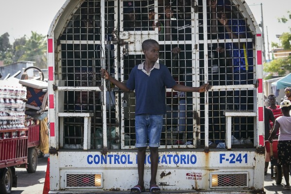 A boy stands on the bumper step of a paddy wagon holding undocumented Haitians detained by immigration officials, in Dajabon, Dominican Republic, Friday, May 17, 2024. As violence and political turmoil grip neighboring Haiti, the Dominican Republic will hold elections Sunday that have been defined by calls for more crackdowns on migrants and finishing a border wall dividing the countries. (AP Photo/Matias Delacroix)
