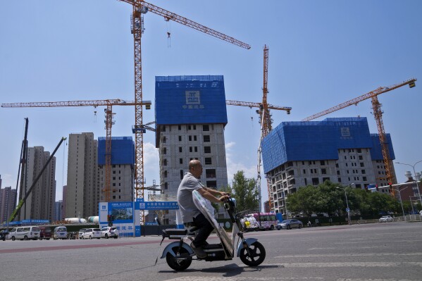 FILE - A man rides on an electric bike past by a residential buildings under construction in Beijing on June 5, 2023. China promised more help for renters as it rolls out a flurry of measures to prop up its ailing property market, while also promising to keep government spending at a “necessary intensity.” (AP Photo/Andy Wong, File)