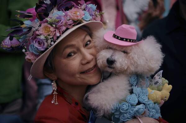 A reveler holding her pet wearing a decorated hat and costume poses for a picture during the annual Easter Parade and Bonnet Festival in front of St. Patrick's Cathedral on Sunday, April 20, 2025, in New York. (AP Photo/Andres Kudacki)