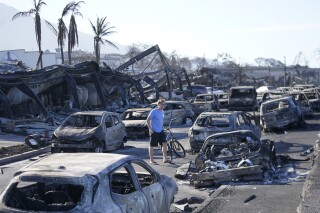 A man walks through wildfire wreckage Friday, Aug. 11, 2023, in Lahaina, Hawaii. Hawaii emergency management records show no indication that warning sirens sounded before people ran for their lives from wildfires on Maui that wiped out a historic town. (AP Photo/Rick Bowmer)