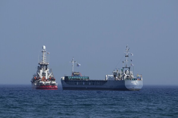 A cargo ship, right, and a ship belonging to the Open Arms aid group, are loaded with 240 tons of canned food destined for Gaza prepare to set sail outside the Cypriot port of Larnaca, Cyprus, on Saturday, March 30, 2024. U.S. charity World Central Kitchen says the ship, named Jennifer, was due to depart following the inaugural voyage of the Cyprus-Gaza sea route earlier this month by the Open Arms vessel that delivered 200 tons of food and water. (AP Photo/Petros Karadjias)