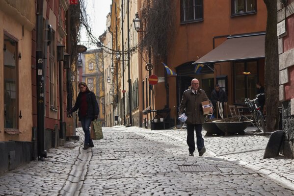 FILE - People walk down a quiet cobbled street in Stockholm, Sweden, Wednesday, March 25, 2020. The streets of Stockholm are quiet but not deserted. People still sit at outdoor cafes in the center of Sweden's capital. Vendors still sell flowers. Teenagers still chat in groups in parks. Some still greet each other with hugs and handshakes. After a long, dark Scandinavian winter, the coronavirus pandemic is not keeping Swedes at home even while citizens in many parts of the world are sheltering in place and won't find shops or restaurants open on the few occasions they are permitted to venture out. (AP Photo/David Keyton, File)