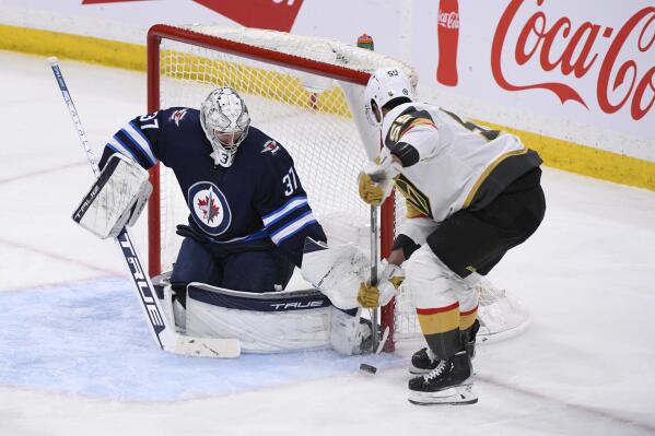 Winnipeg Jets goaltender Connor Hellebuyck (37) makes a save on Vegas Golden Knights' Keegan Kolesar (55) during the third period of an NHL hockey game in Winnipeg, Manitoba, Tuesday, March 22, 2022. (Fred Greenslade/The Canadian Press via AP)