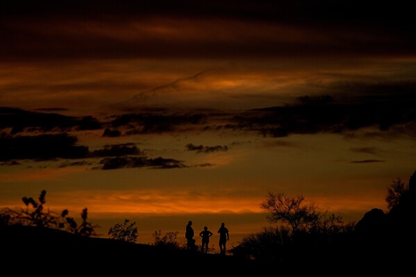 People stand atop a rock formation to watch the sunset, Sunday, July 30, 2023, in Phoenix. Phoenix hit its 31st consecutive day of at least 110 degrees Fahrenheit (43.3 Celsius). The National Weather Service said the temperature climbed to a high of 111 degrees Fahrenheit before the day was through. (AP Photo/Matt York)